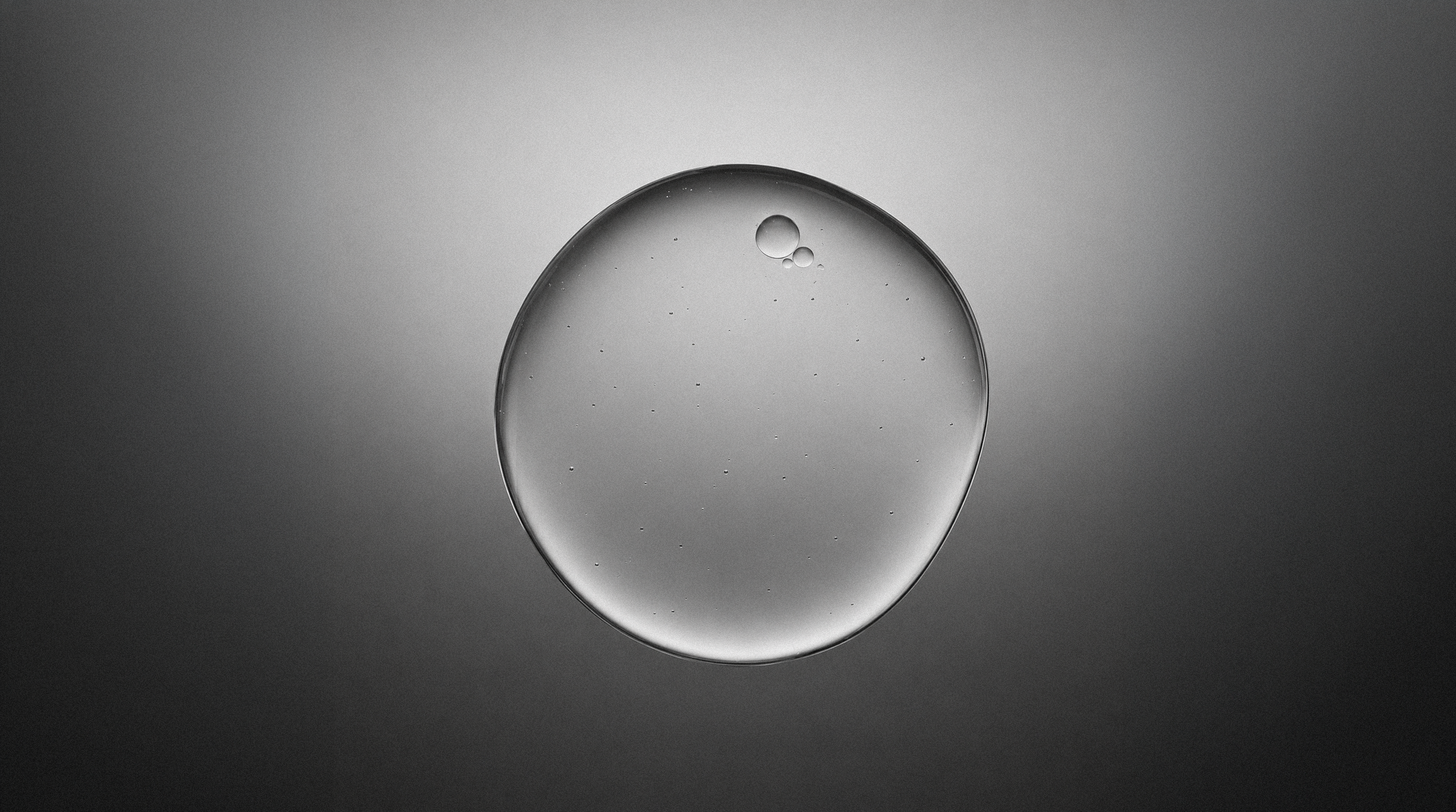 Transparent gel droplet with tiny air bubbles on a dark gradient background